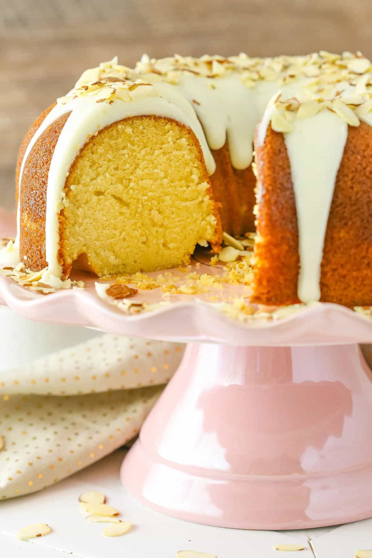 An almond amaretto bundt cake on a pink cake stand with a few slices removed.