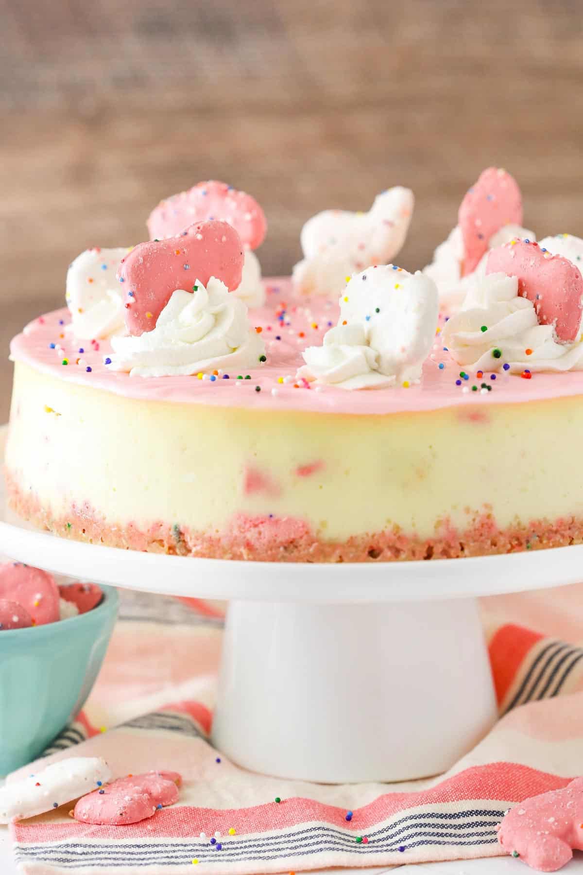 Close up of a frosted animal cookie cheesecake on a white cake stand.