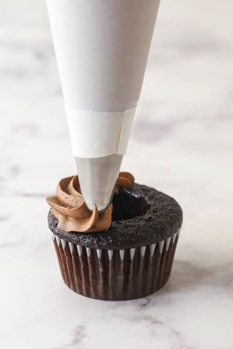 Piping chocolate buttercream around the edge of a cored chocolate cupcake.