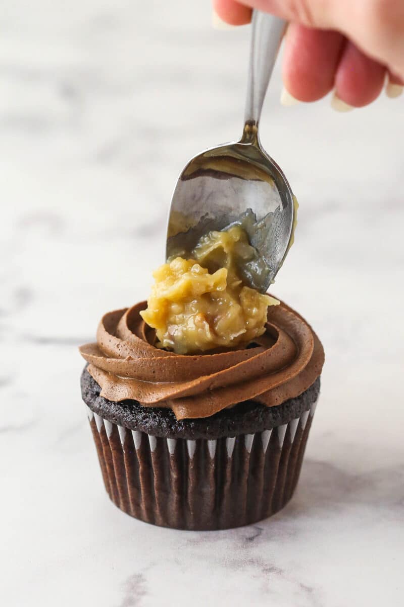 Spooning coconut-pecan filling on top of a German chocolate cupcake.