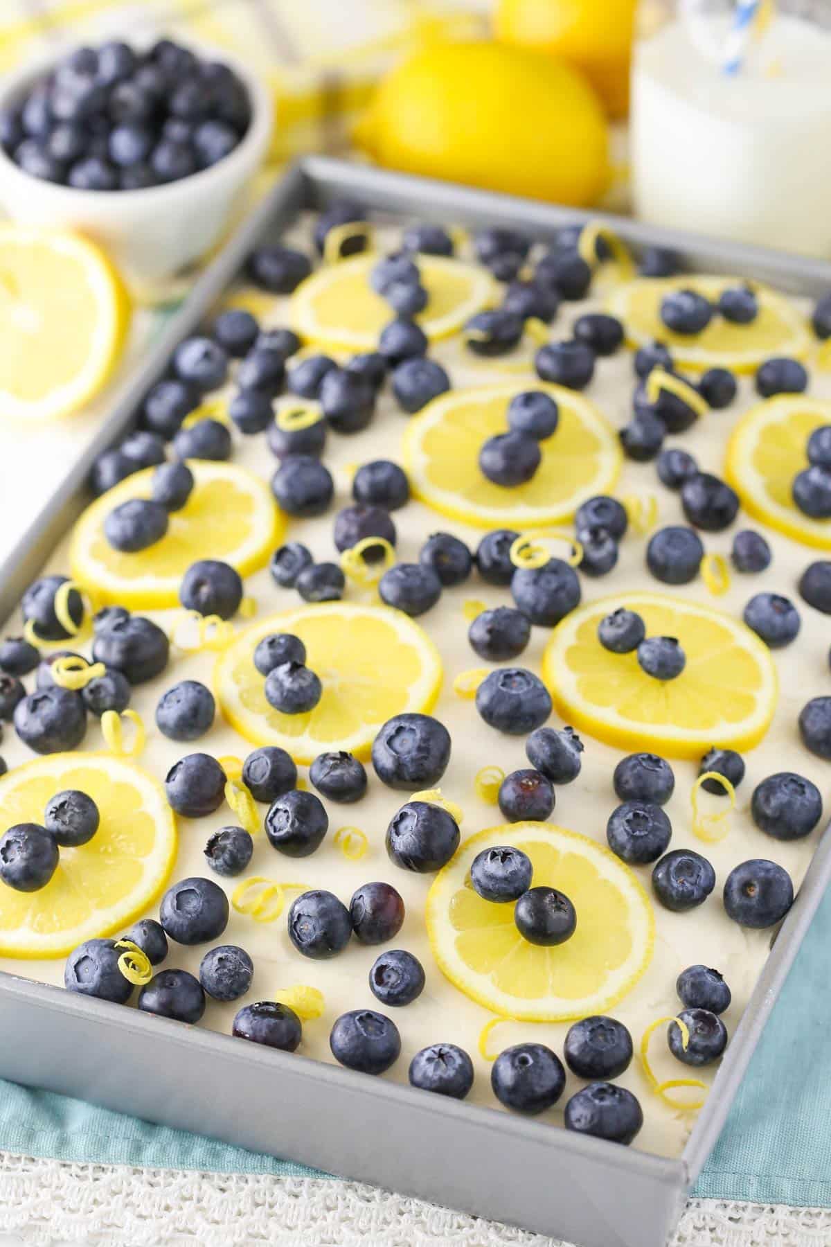 A fully decorated lemon blueberry poke cake in a metal pan.