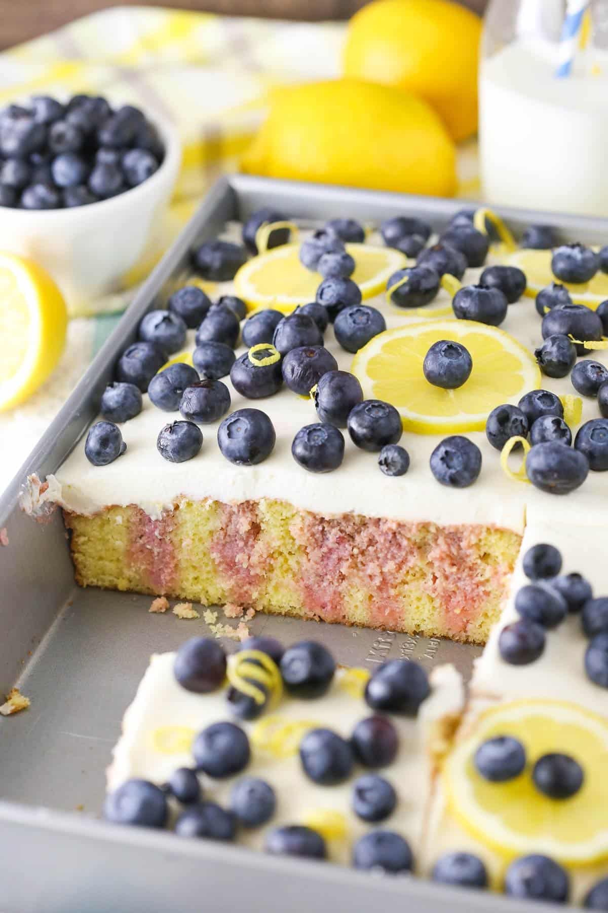 A lemon blueberry poke cake with several slices removed from the pan to show inside.