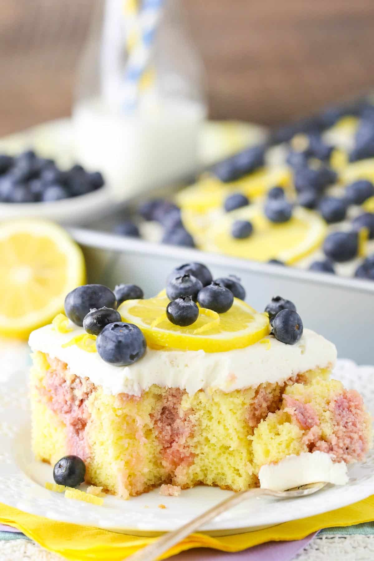 A slice of lemon blueberry poke cake with a bite removed.