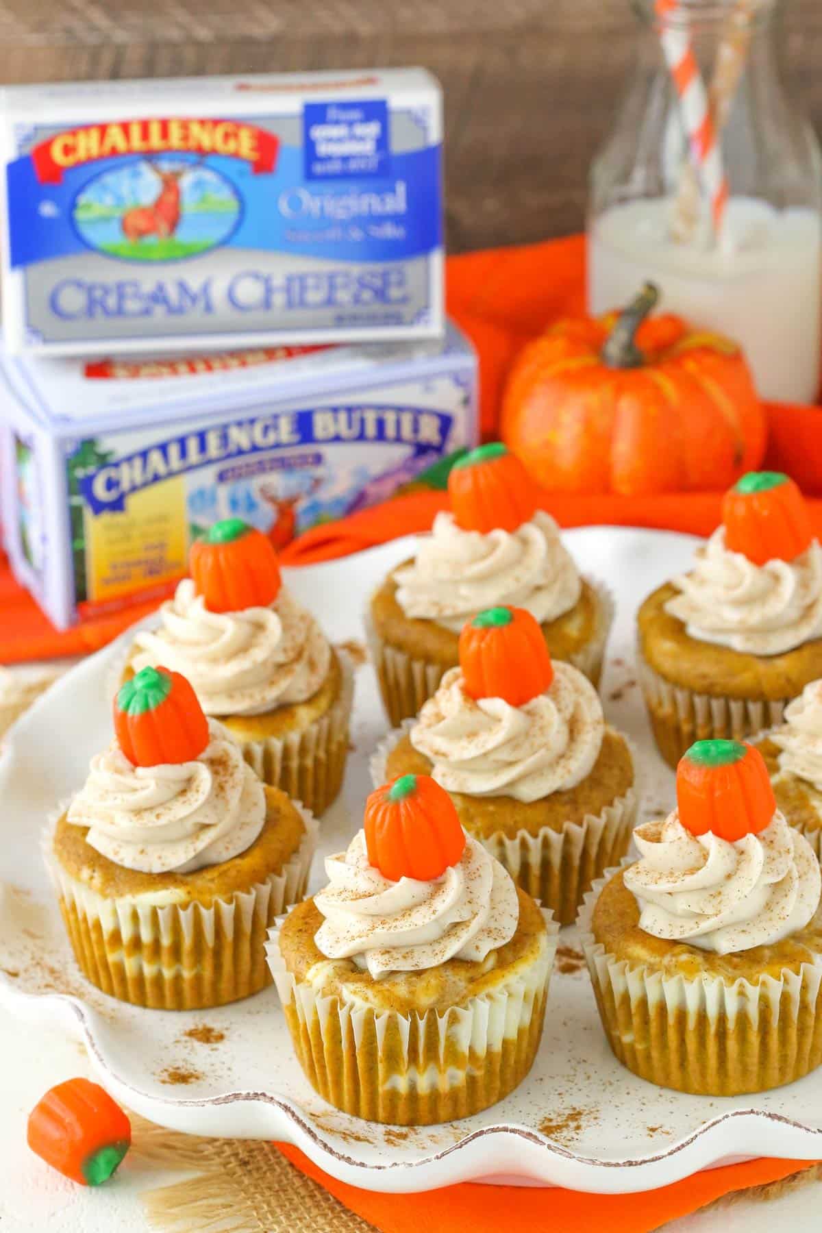 Pumpkin cheesecake swirl cupcakes on a white platter next to cream cheese and butter. 