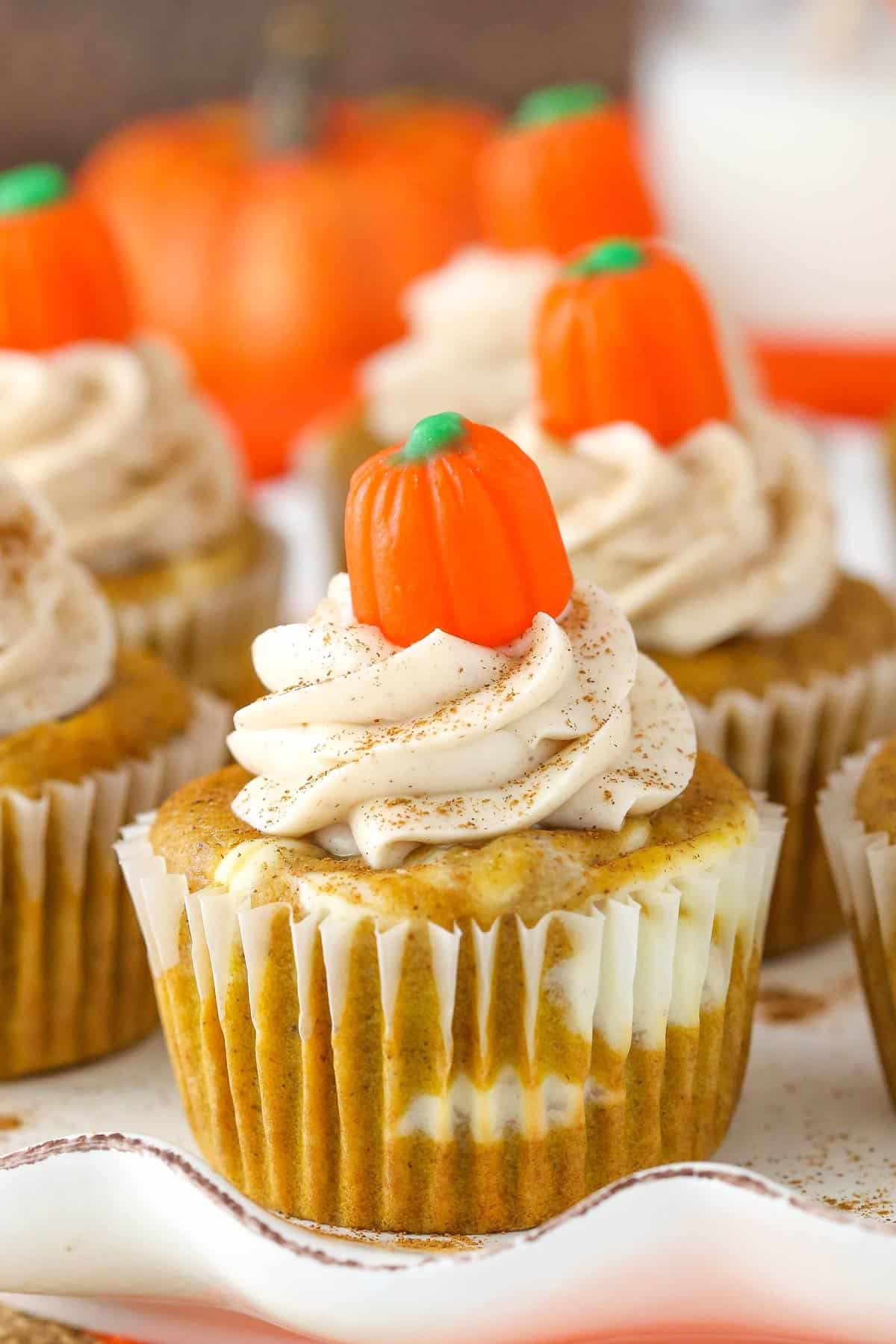 These easy pumpkin cheesecake swirl cupcakes are a fun combination of moist pumpkin cake and creamy pumpkin cheesecake! Perfect for fall! A pumpkin cheesecake swirl cupcake on a platter.