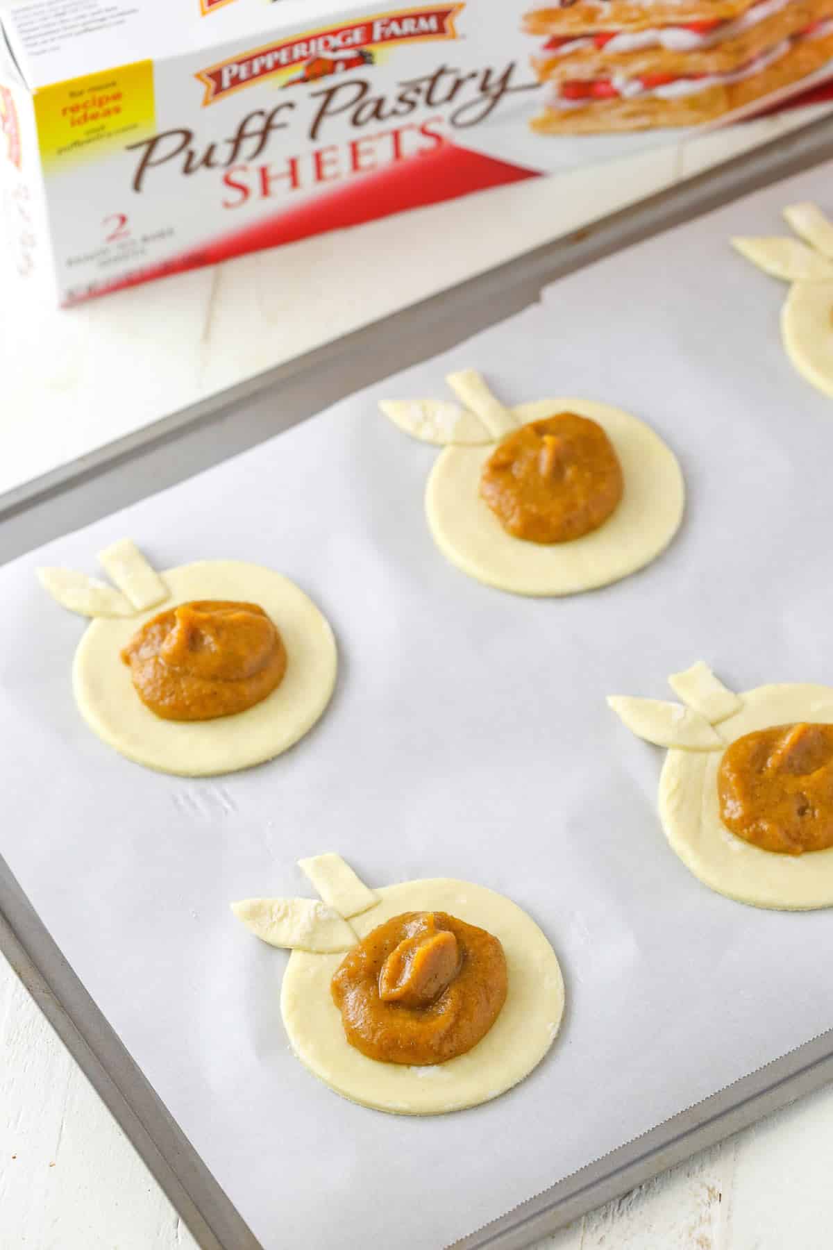 Pumpkin spice pumpkin pastries without their top piece on a baking sheet.