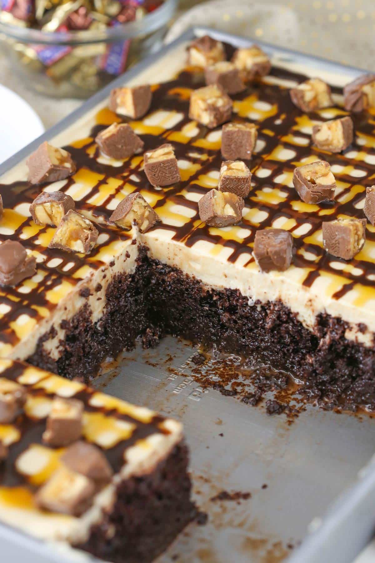 A snickers poke cake with several slices missing to show layers.