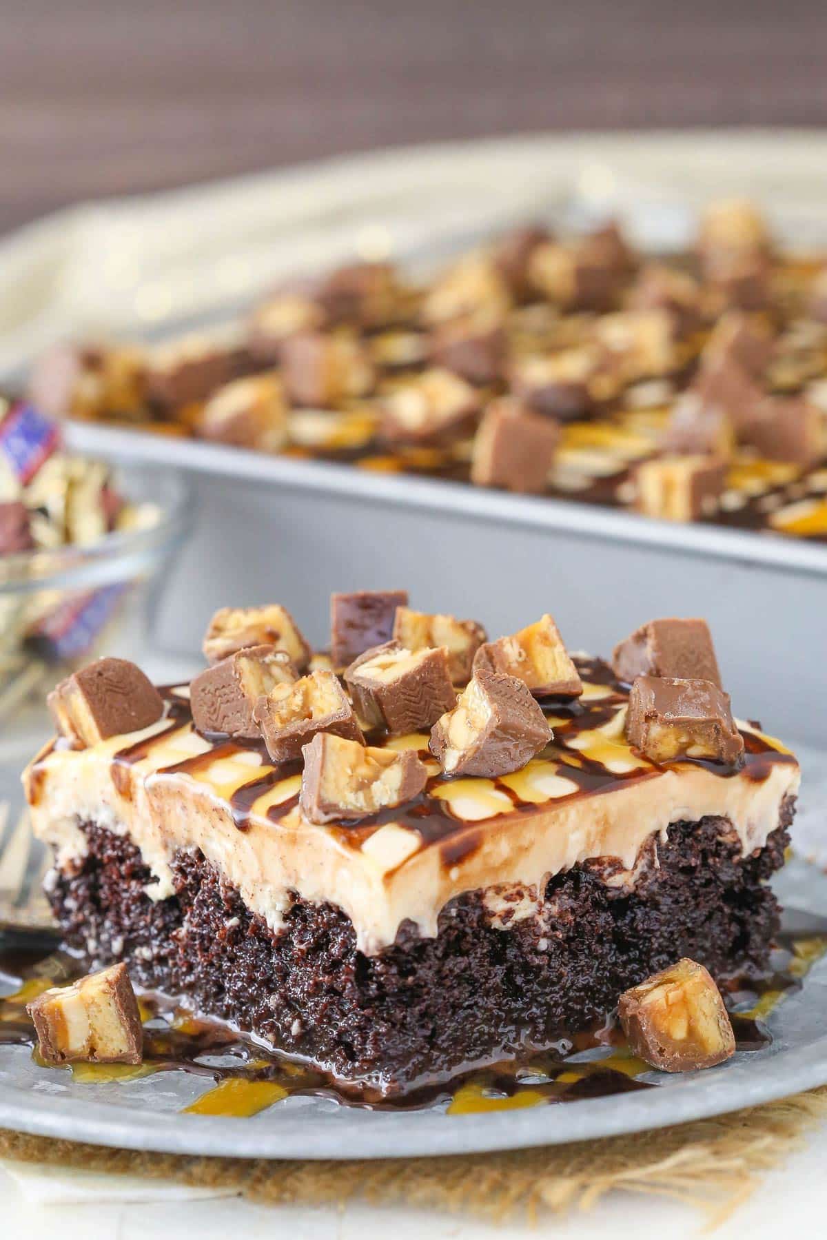 A slice of snickers poke cake on a silver plate.