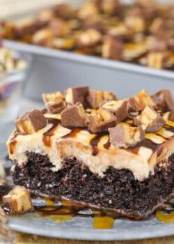 Close up of a slice of snickers poke cake on a silver plate.
