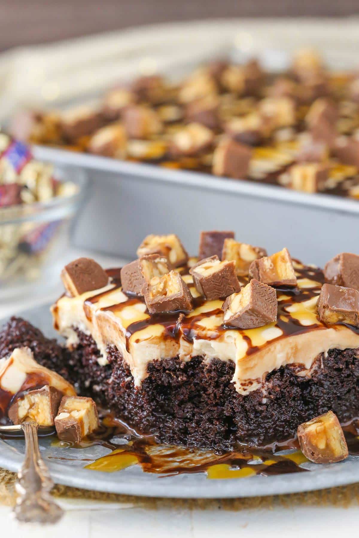 A slice of snickers poke cake with a bite removed on a fork.