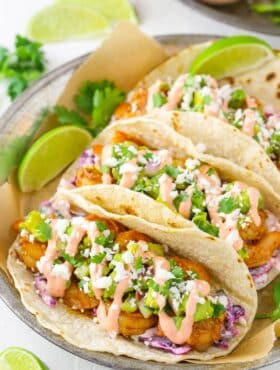 Three spicy sriracha shrimp tacos on a silver plate.