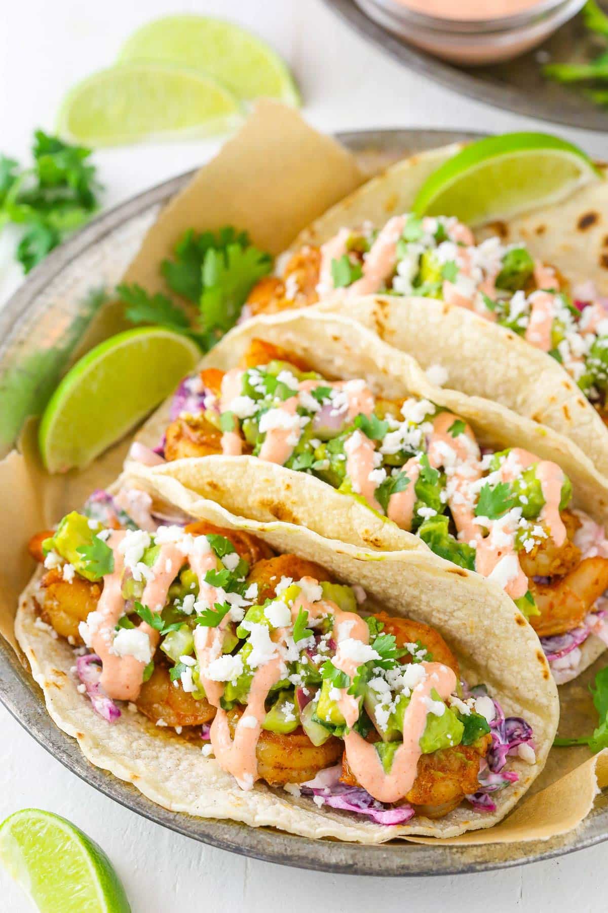 Three spicy sriracha shrimp tacos on a silver plate.