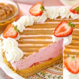 A strawberry dulce de leche ice cream pie in a pie plate with a slice missing to show interior of pie.