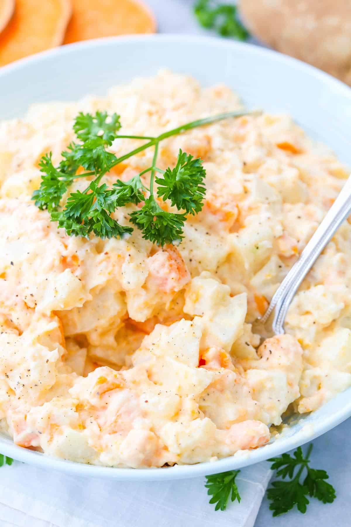 A bowl of three potato salad with a spoon inserted.