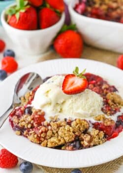 A bowl of triple berry crisp with ice cream and a strawberry on top.