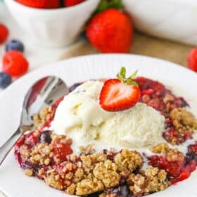 A bowl of triple berry crisp with ice cream and a strawberry on top.
