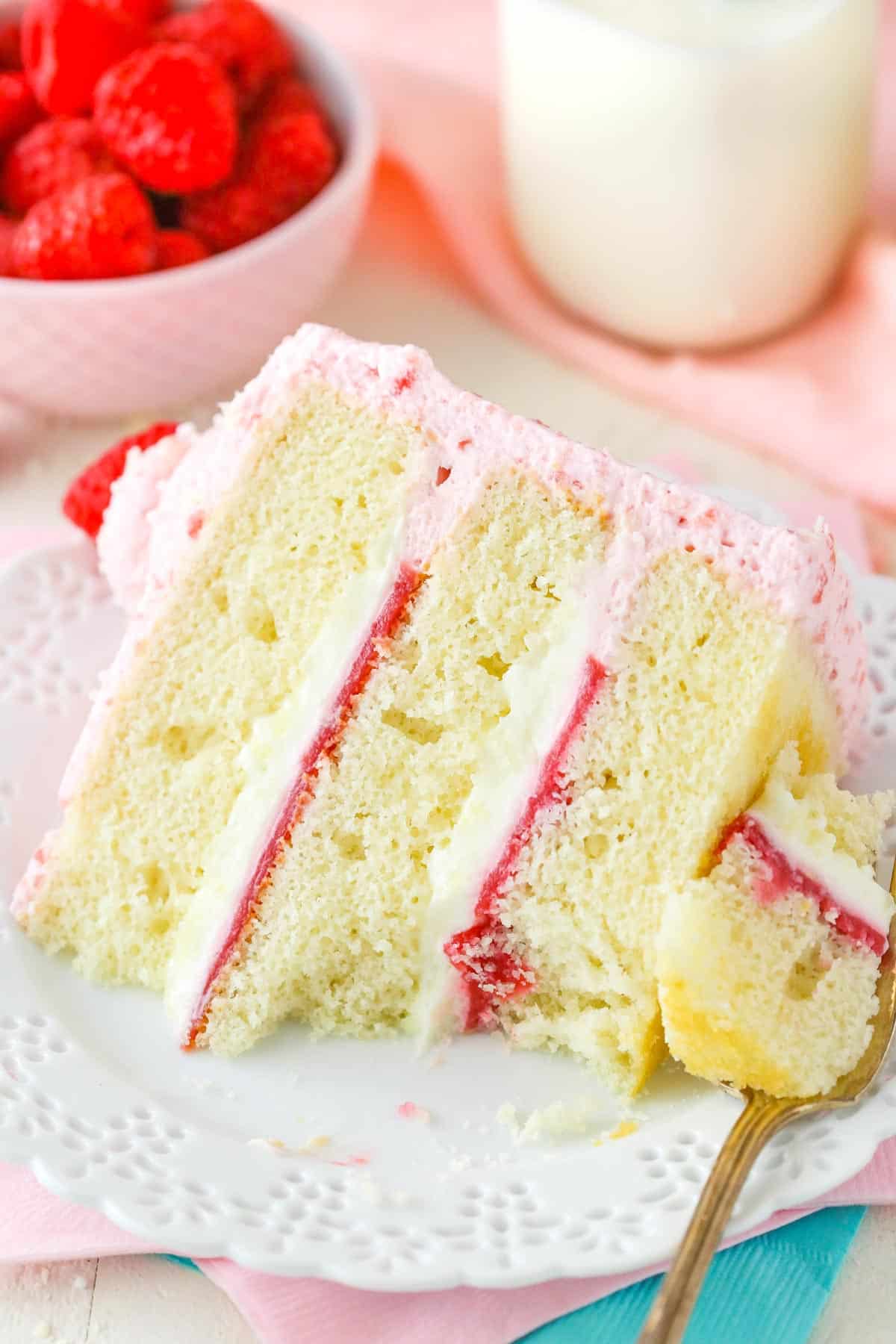 A slice of white chocolate raspberry mousse cake with a bite removed on a fork.