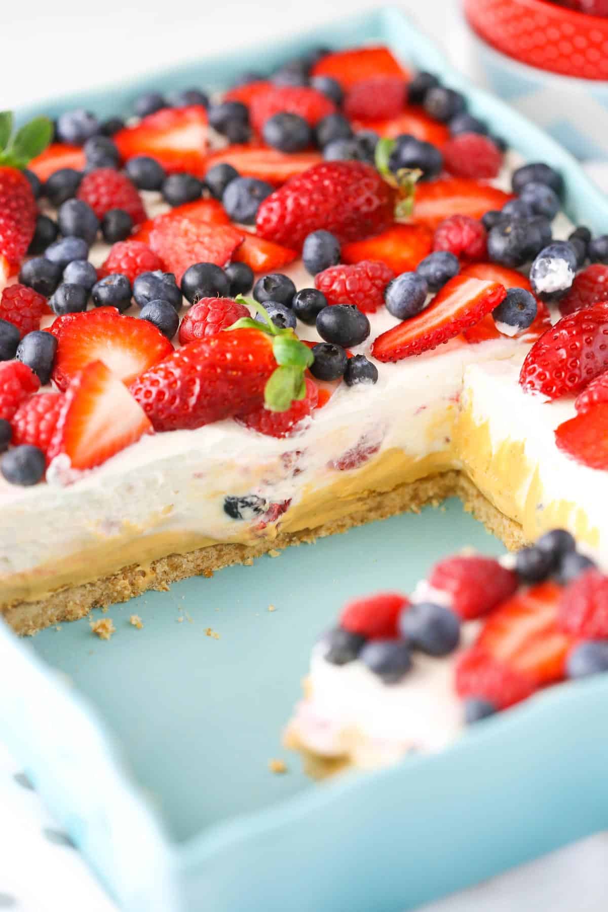 A teal baking dish filled with berries and cream layer dessert.