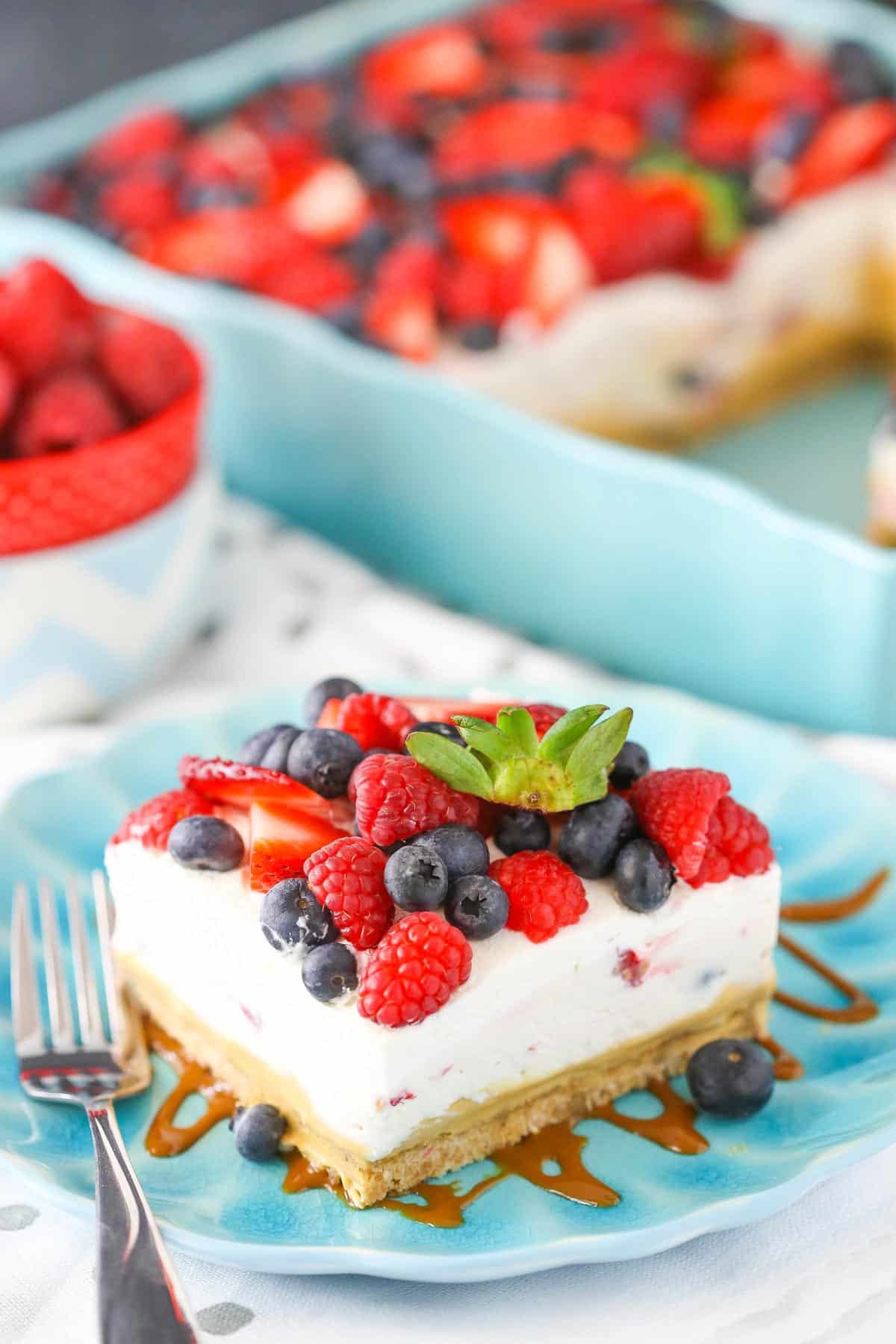 A slice of berries and cream layer dessert on a teal plate.