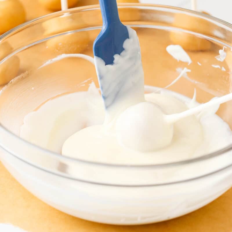 A cookie pop being dipped in white candy coating.