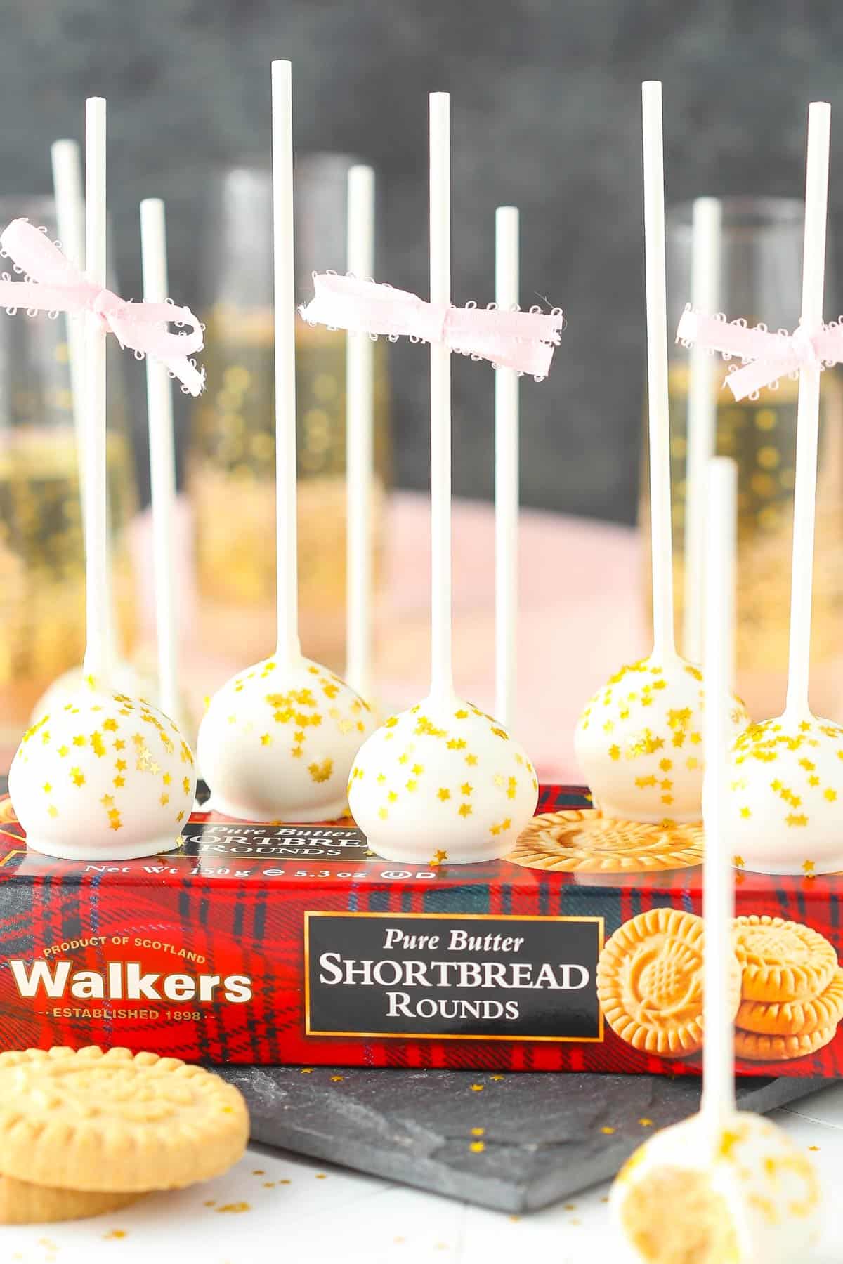 Several no bake champagne cookie pops on top of a box of shortbread.