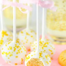 Several no bake champagne cookie pops on a pink napkin with a bite taken from first pop.