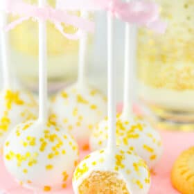 Several no bake champagne cookie pops on a pink napkin with a bite taken from first pop.