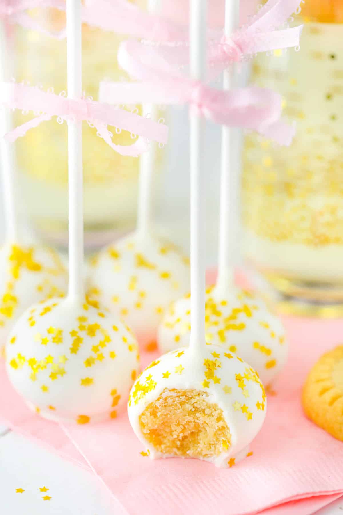 Several no bake champagne cookie pops on a pink napkin with a bite taken from first pop.
