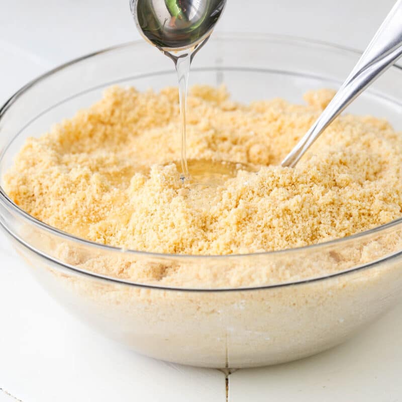 Corn syrup being drizzle into a bowl of no bake champagne cookie pop filling mixture.