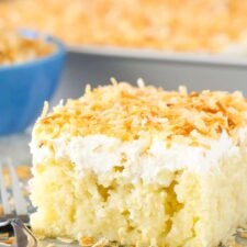 A slice of coconut poke cake on a silver plate next to a fork.