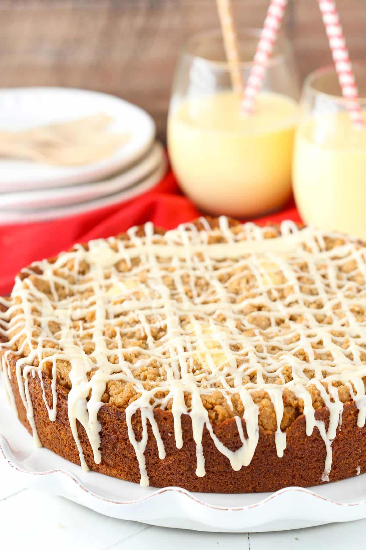 An eggnog crumb cake on a white platter with eggnog in the background.