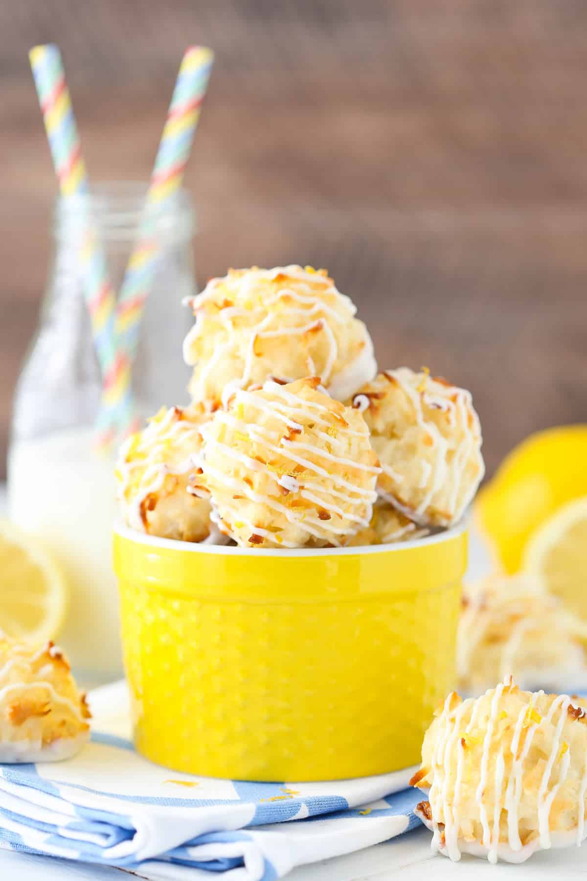 A yellow container filled with lemon coconut macaroons with more cookies surrounding it.