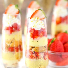 Several mini strawberry champagne trifles next to a bowl of strawberries.