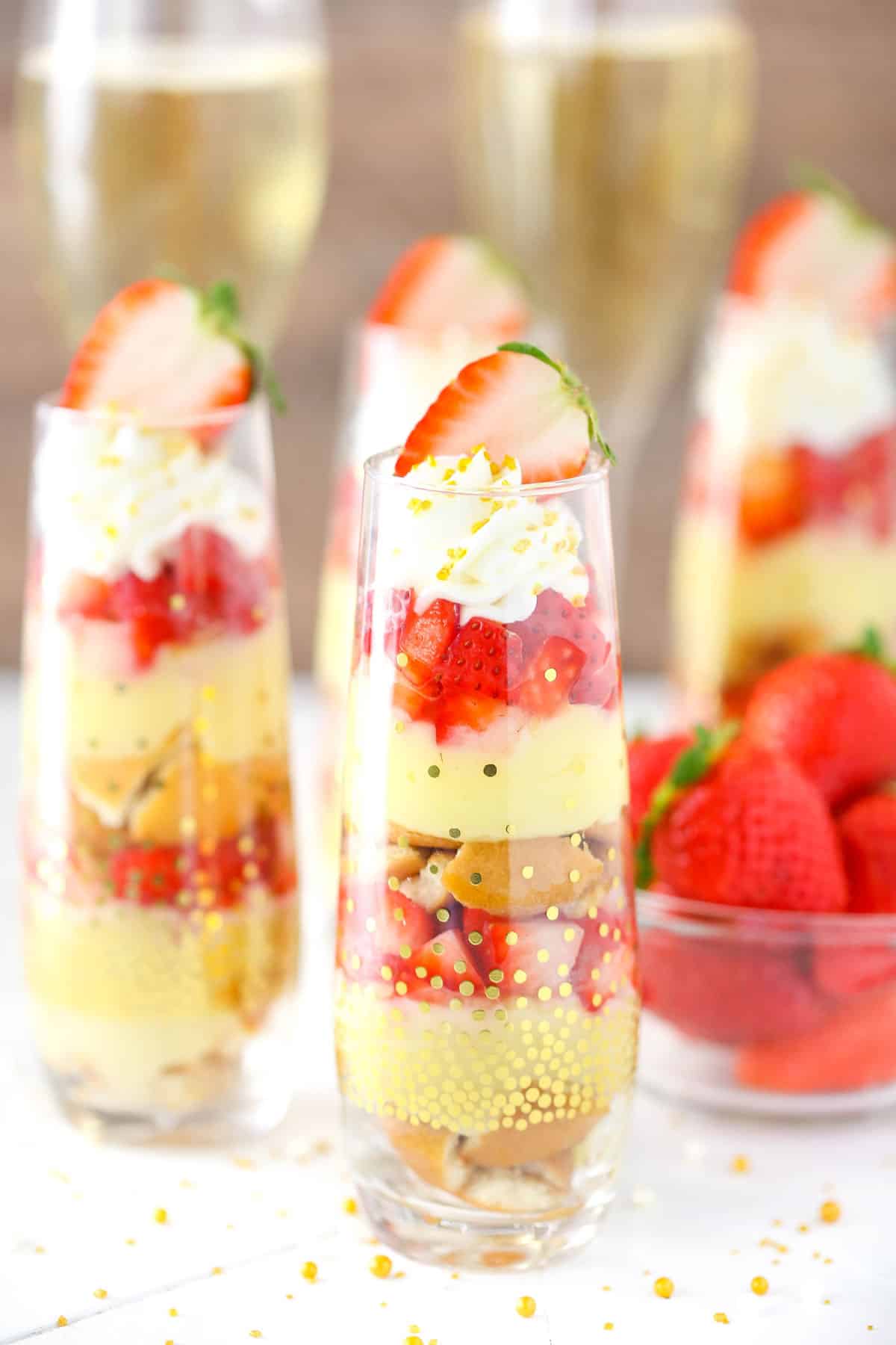 Several mini strawberry champagne trifles next to a bowl of strawberries.