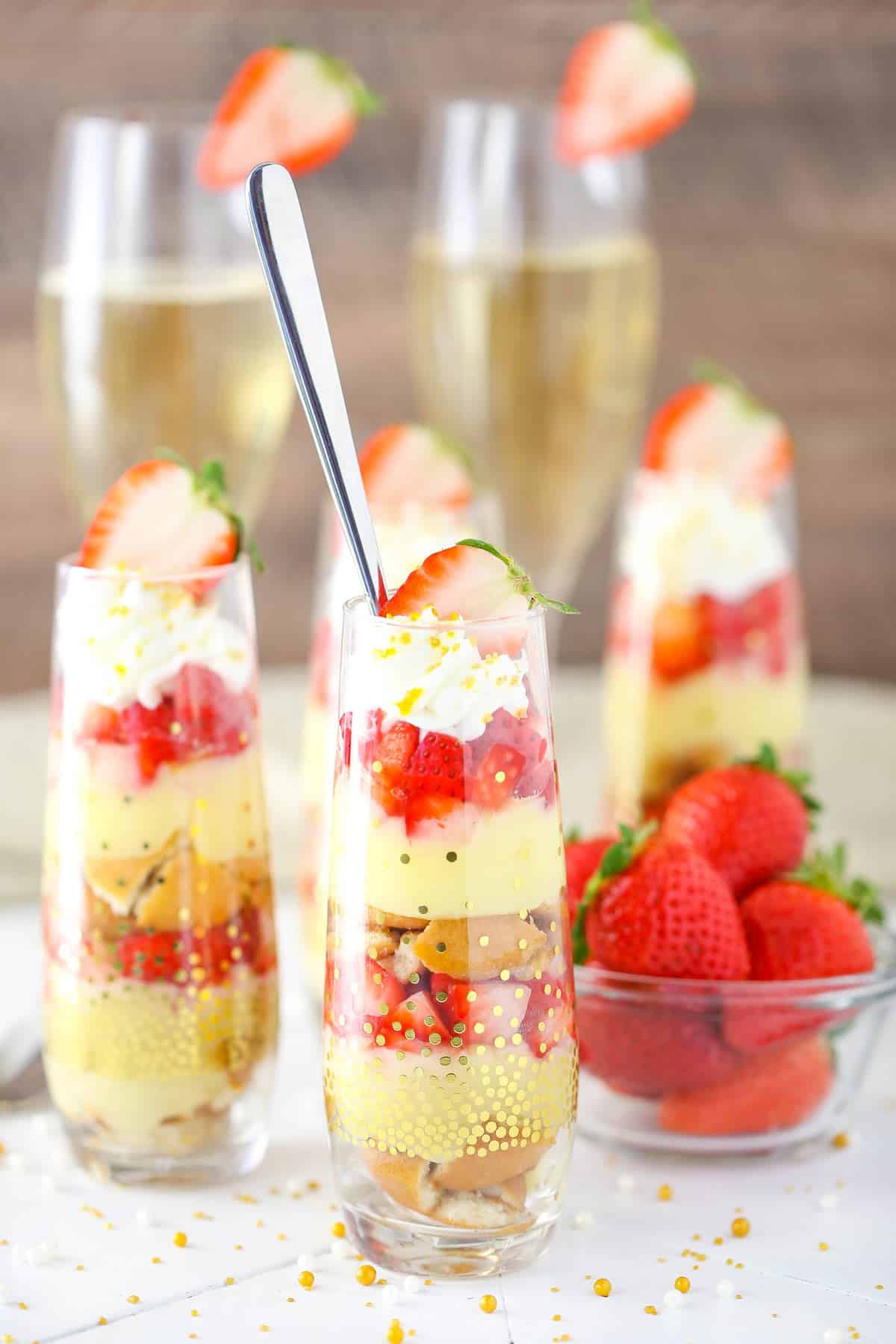 A few mini strawberry champagne trifles next to a bowl of strawberries.