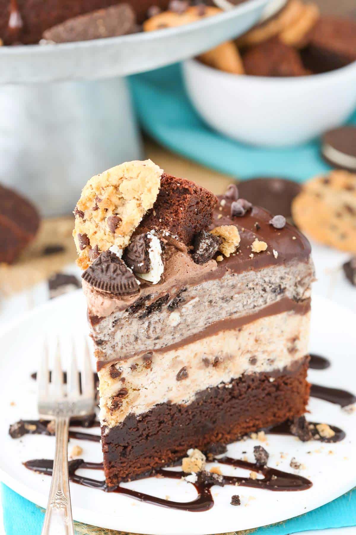 Oreo brookie ice cream cake is made of fudgy brownie topped with chocolate chip cookie ice cream, chocolate ganache, and Oreo ice cream. A slice of Oreo brookie ice cream cake on a white plate.