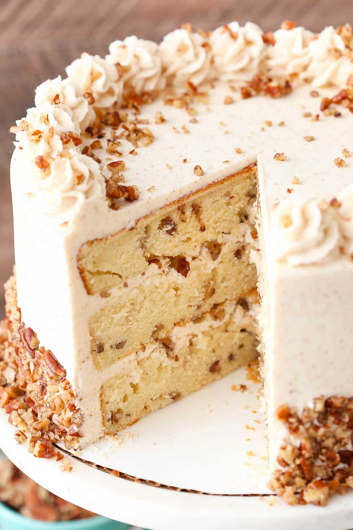A browned butter pecan layer cake on a white cake stand with a slice removed to show interior layers.