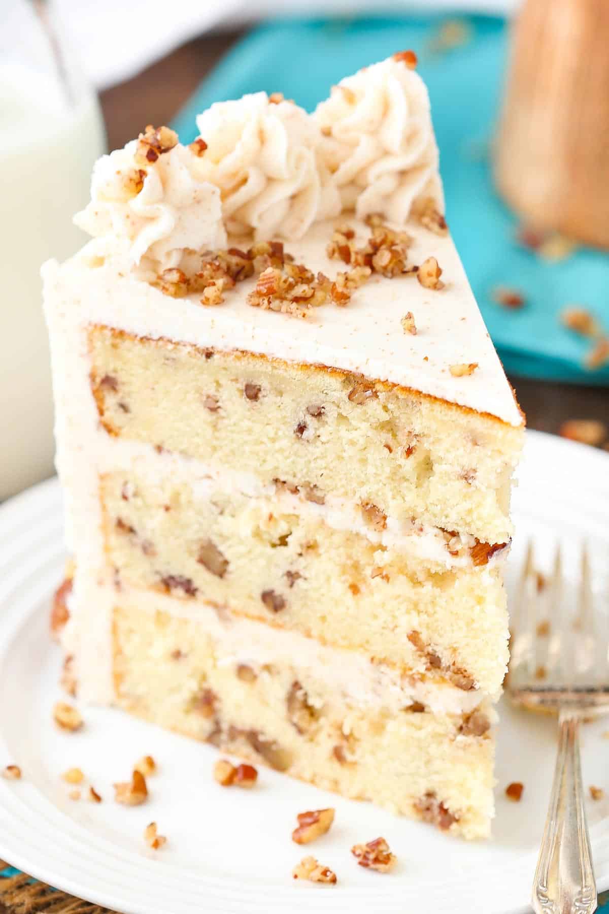 A tall slice of browned butter pecan layer cake on a white plate.