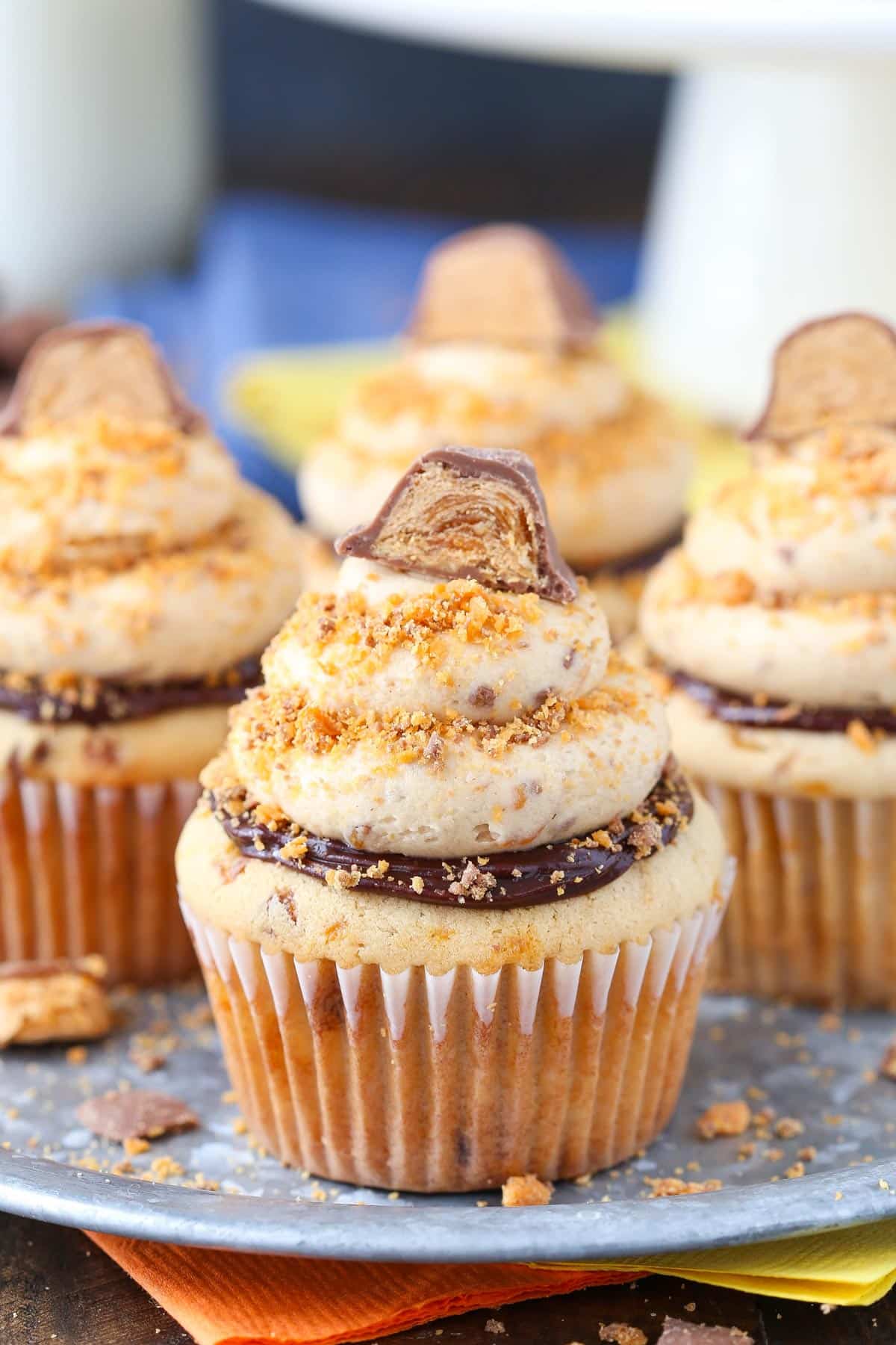 Every bite of these Butterfinger Cupcakes is loaded with crushed Butterfingers, from the moist peanut butter cupcakes to the frosting. Close up of Butterfinger Cupcakes on a silver plate.