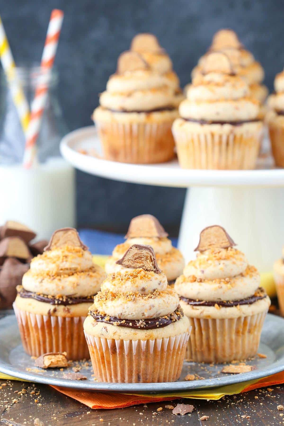 Four Butterfinger Cupcakes on a silver plate with more cupcakes in the background.
