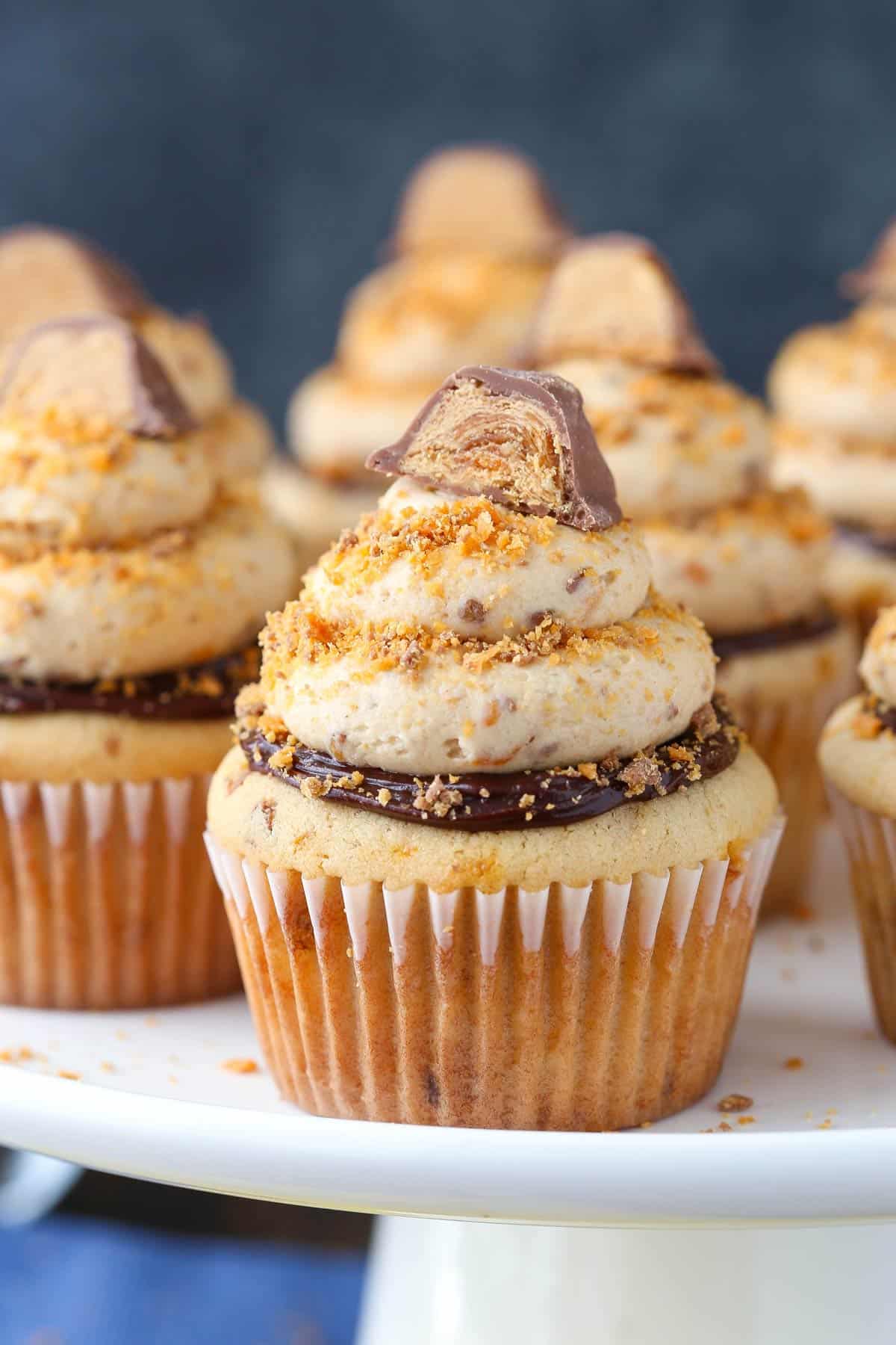 Close up of a Butterfinger Cupcake on a white cake stand.