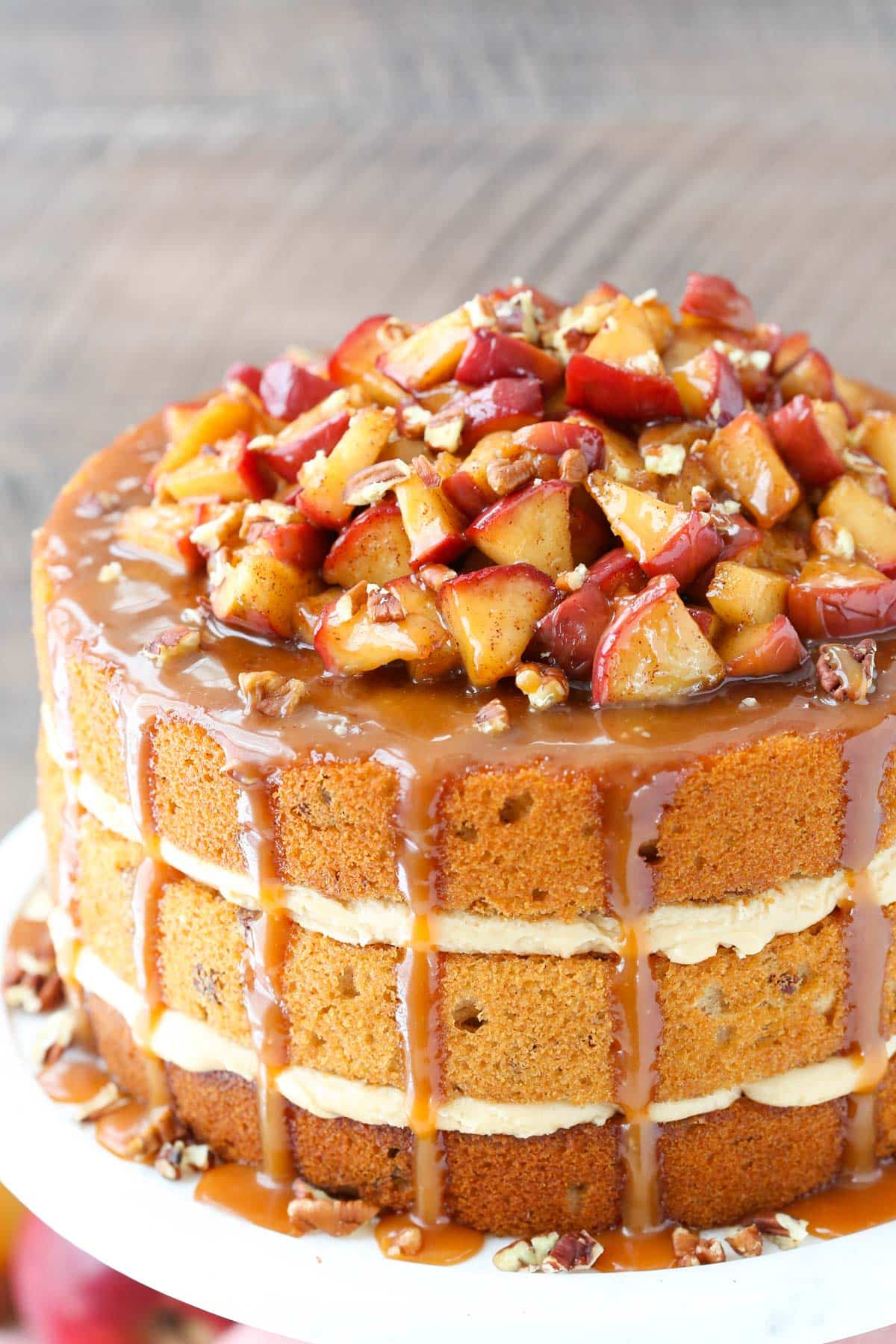 Close up of a caramel apple pecan layer cake on a white cake stand piled high with apples.
