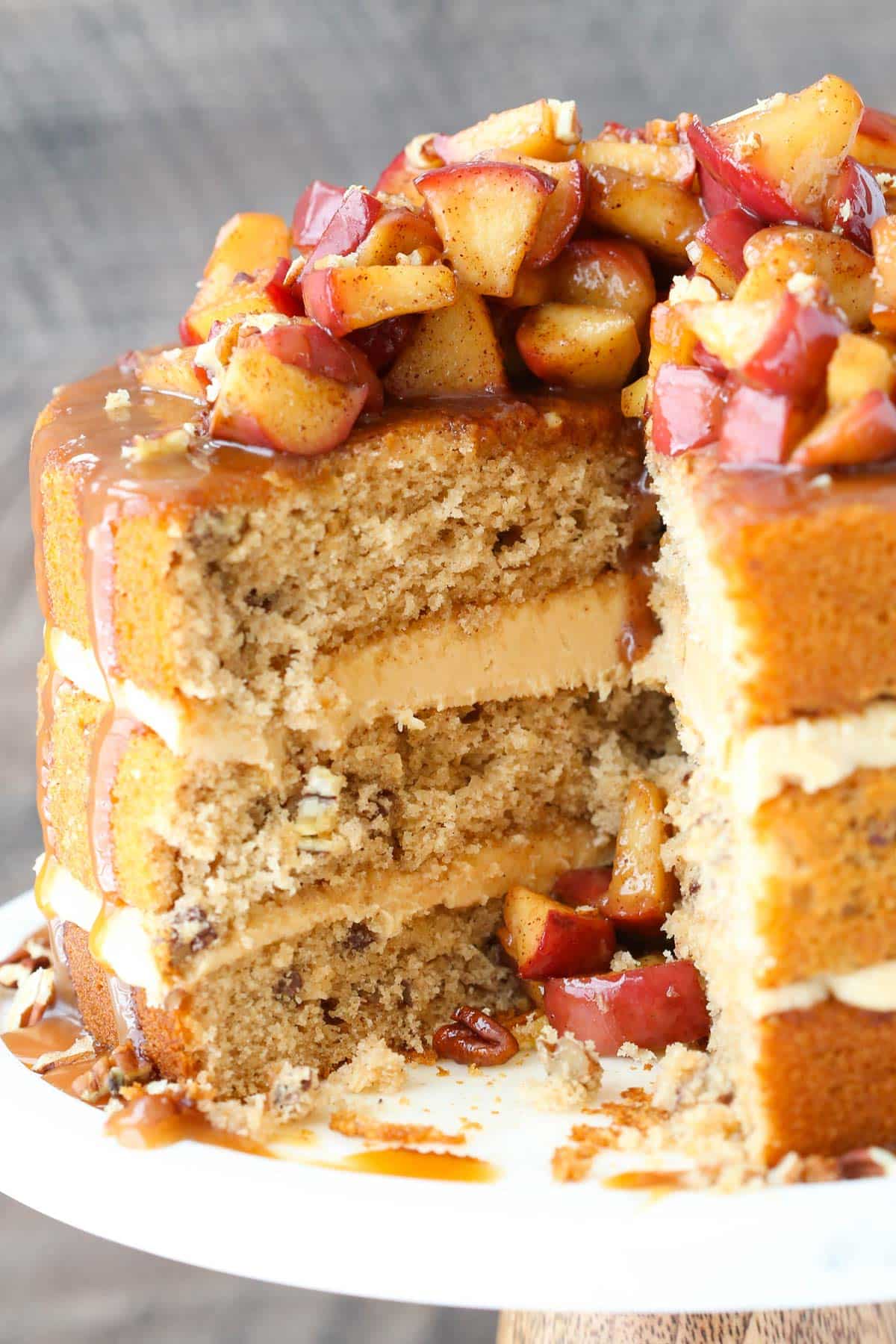 A caramel apple pecan layer cake on a white cake stand with a slice removed to show interior layers.