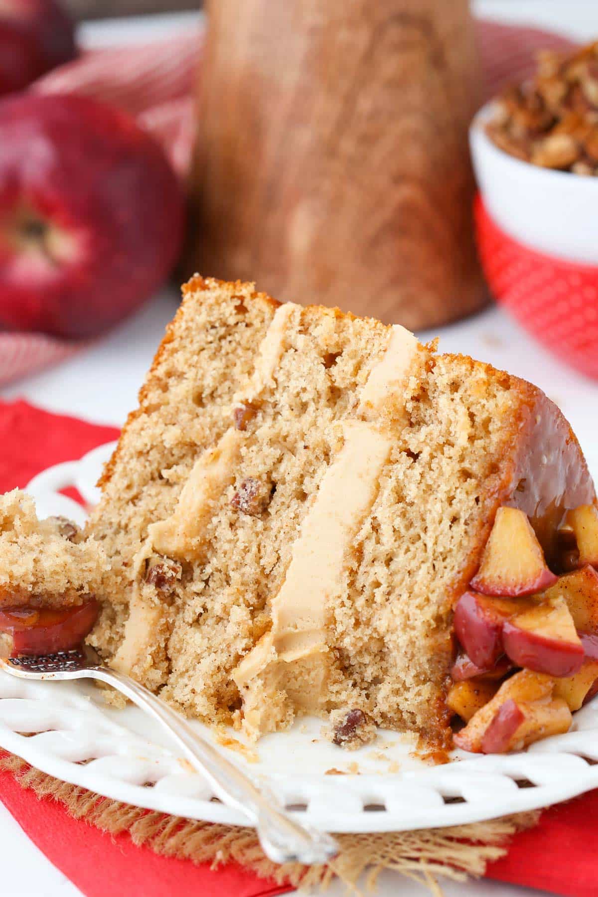 A slice of caramel apple pecan layer cake laying on its side on a plate with a bite removed.