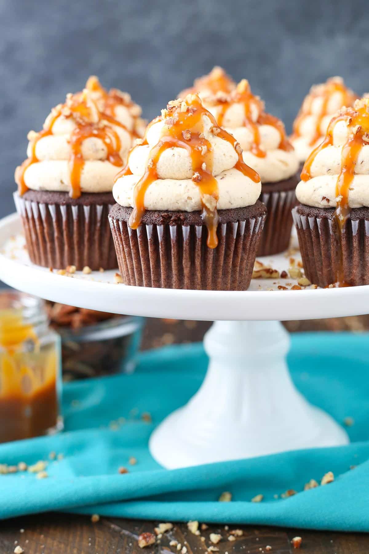 Side view of chocolate turtle cupcakes on a white cake stand.