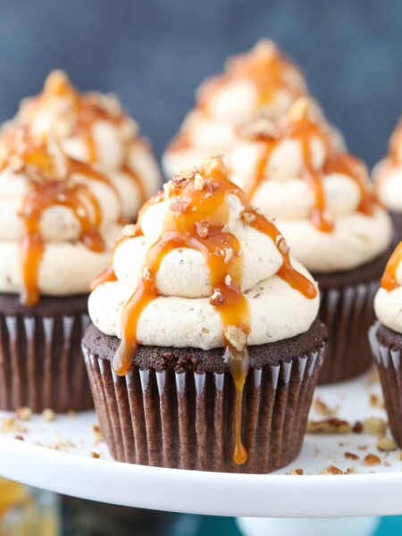 Close up of chocolate turtle cupcakes on a white cake stand.