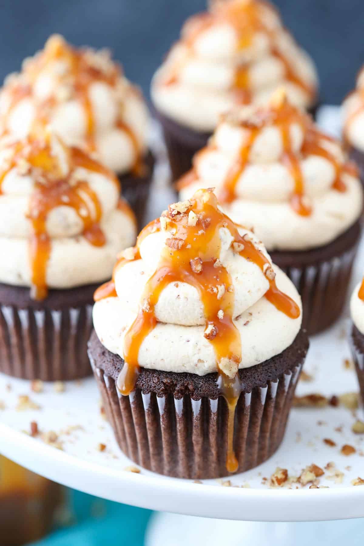 Close up of a chocolate turtle cupcake on a white cake stand.