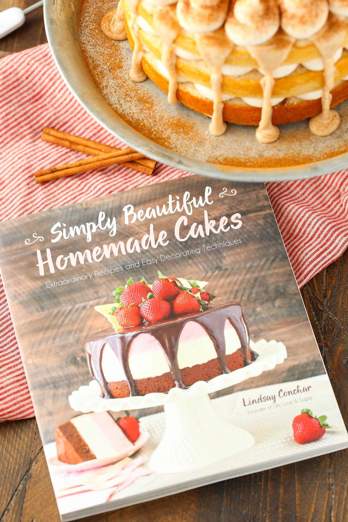 Close up of a cookbook with a cinnamon roll layer cake in the background.