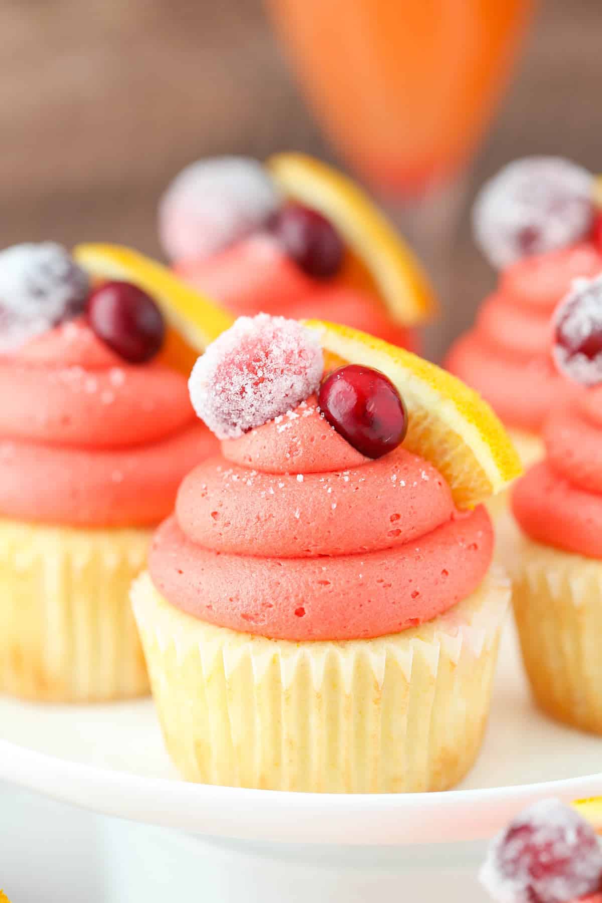 Close up of a cranberry mimosa cupcake on a white cake stand.
