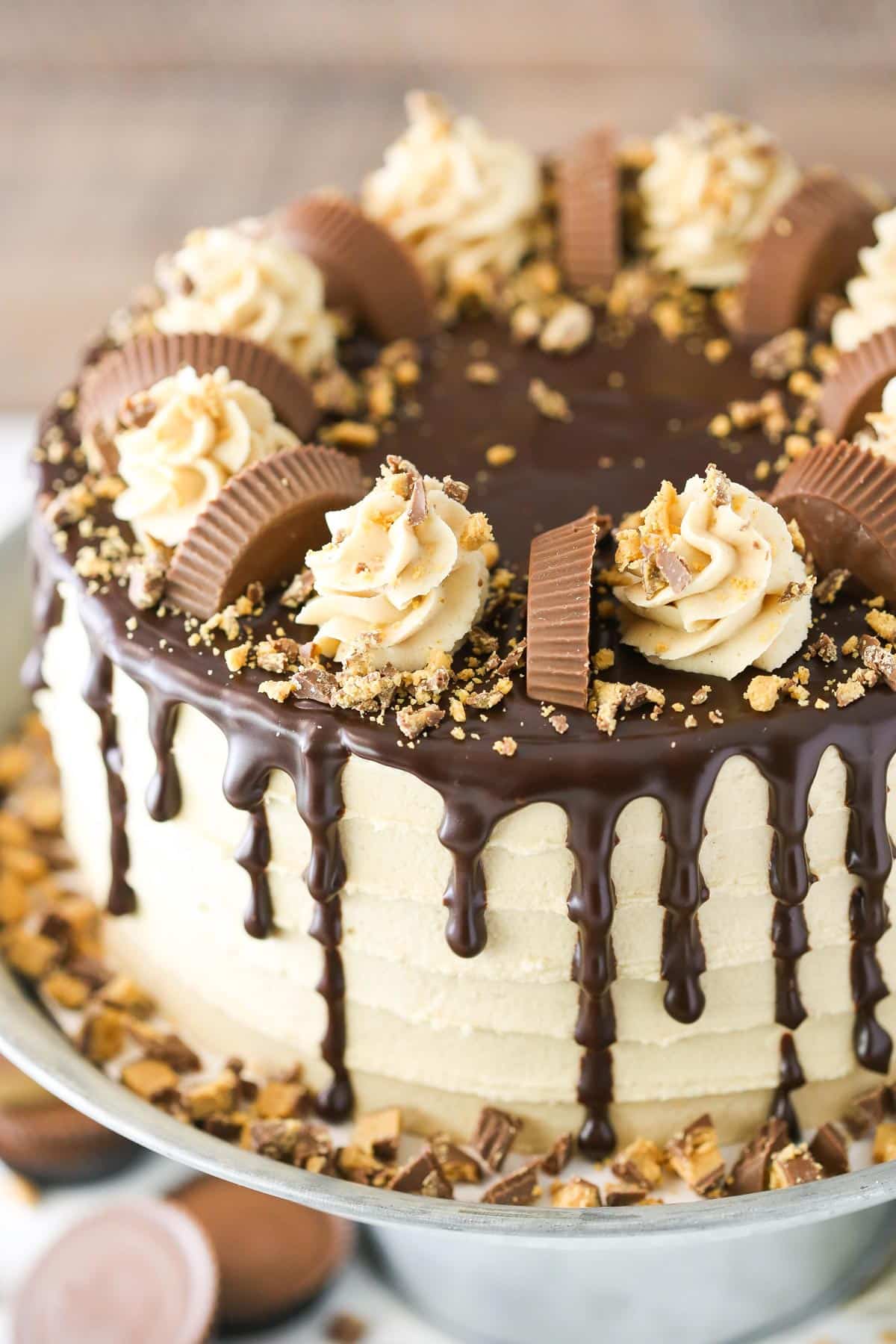This peanut butter chocolate cake is made with layers of moist chocolate cake, peanut butter frosting and chopped Reese’s peanut butter cups. Top view of a peanut butter chocolate layer cake on a silver cake stand.